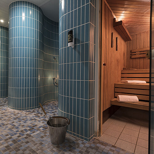 Saunabereich im Maritim proArte Hotel Berlin mit traditionellen Holz-Saunabänken, blauen Fliesen und modernen Duschen.