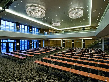 Moderner Saal im Maritim Hotel Düsseldorf mit Reihenbestuhlung, großen Fenstern und beeindruckenden Kronleuchtern.
