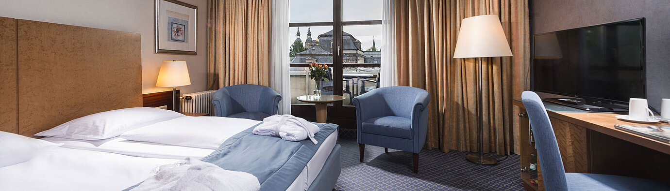 Elegantes Superior Zimmer im Maritim Hotel Fulda mit Doppelbett, Sitzbereich und Balkon mit Blick auf die Stadt.