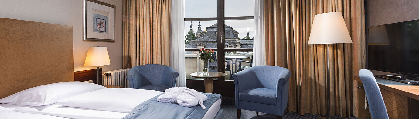 Elegantes Superior Zimmer im Maritim Hotel Fulda mit Doppelbett, Sitzbereich und Balkon mit Blick auf die Stadt.