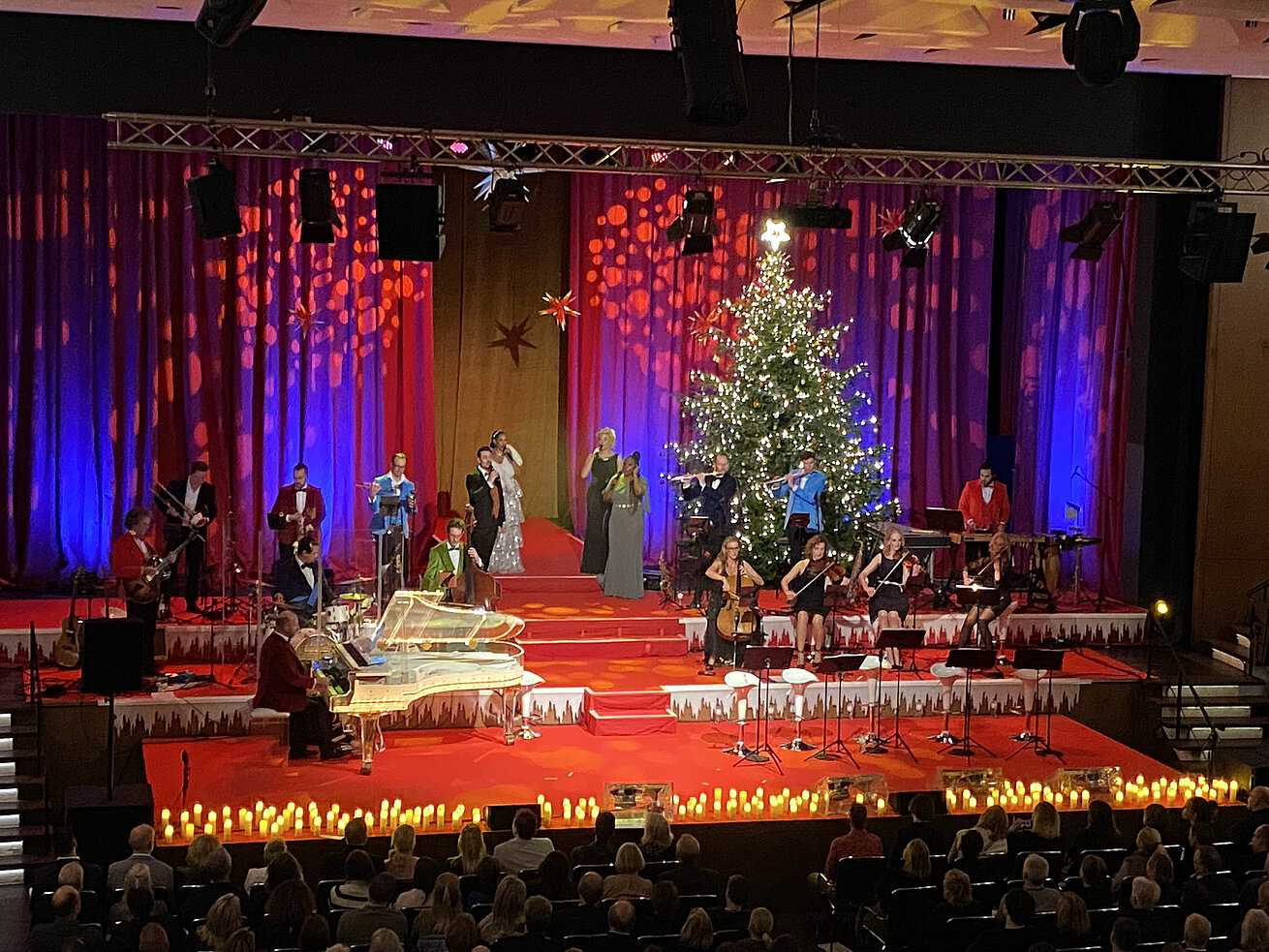 Festlich geschmückte Bühne mit Musikerinnen und Musikern beim Max & Friends Weihnachtskonzert vor großem Publikum.