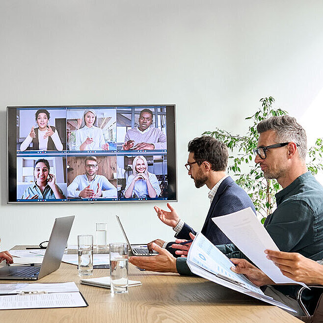 Geschäftsteam in Videokonferenz mit Kollegen auf großem Bildschirm