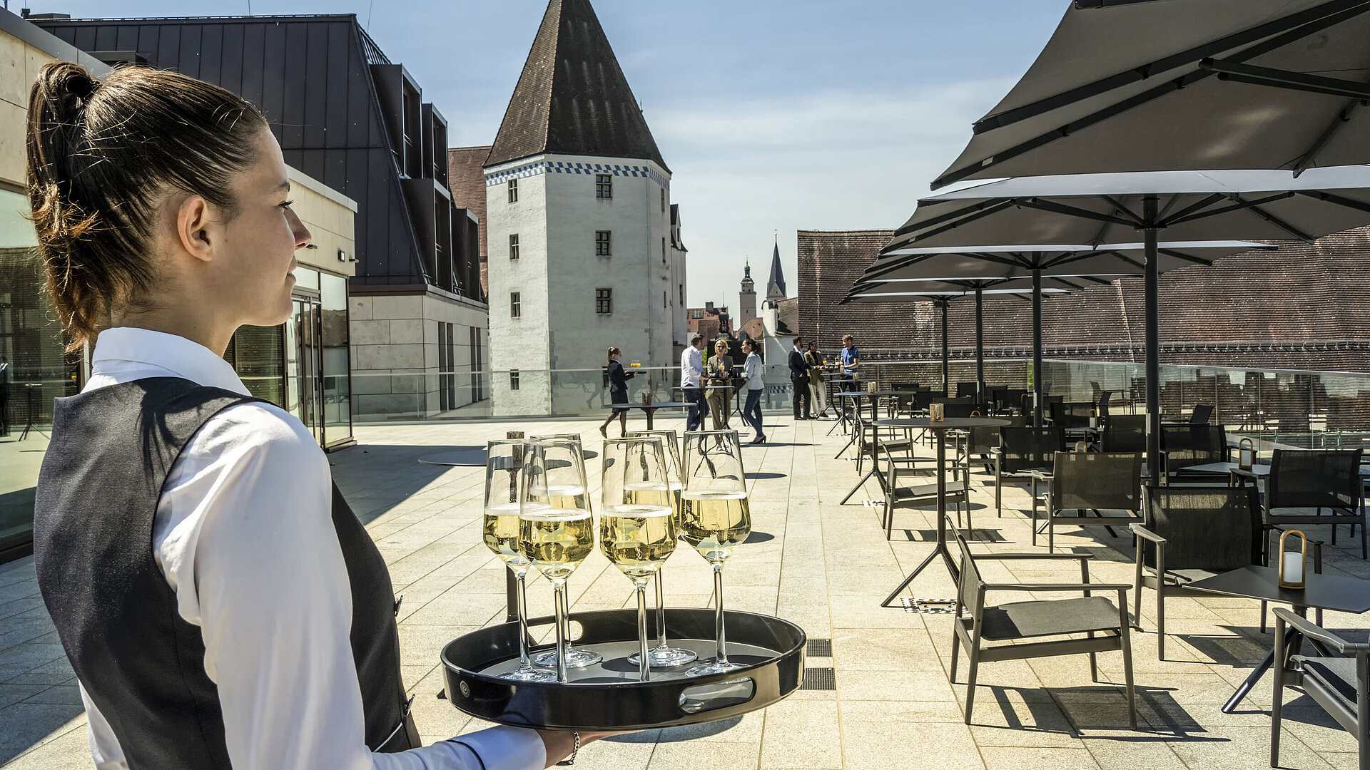 Terrasse Kellnerin serviert Getränke auf der sonnigen Dachterrasse im Maritim Hotel Ingolstadt.
