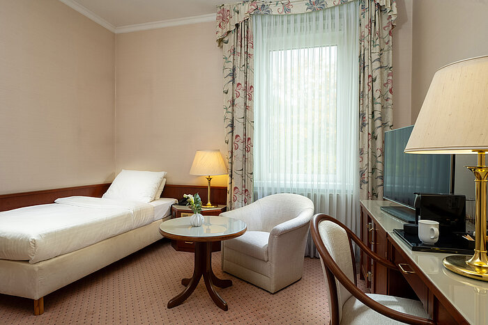 Classic Einzelzimmer Classic Einzelzimmer mit Bett, Sitzecke, Schreibtisch und großem Fenster im hellen, klassischen Design im Maritim Hotel Bad Wildungen.