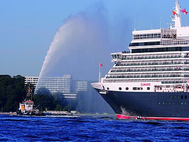 Außenansicht des Maritim Hotels Kiel, im Vordergrund das Kreuzfahrtschiff Queen Elizabeth und ein Schlepper auf dem Wasser.