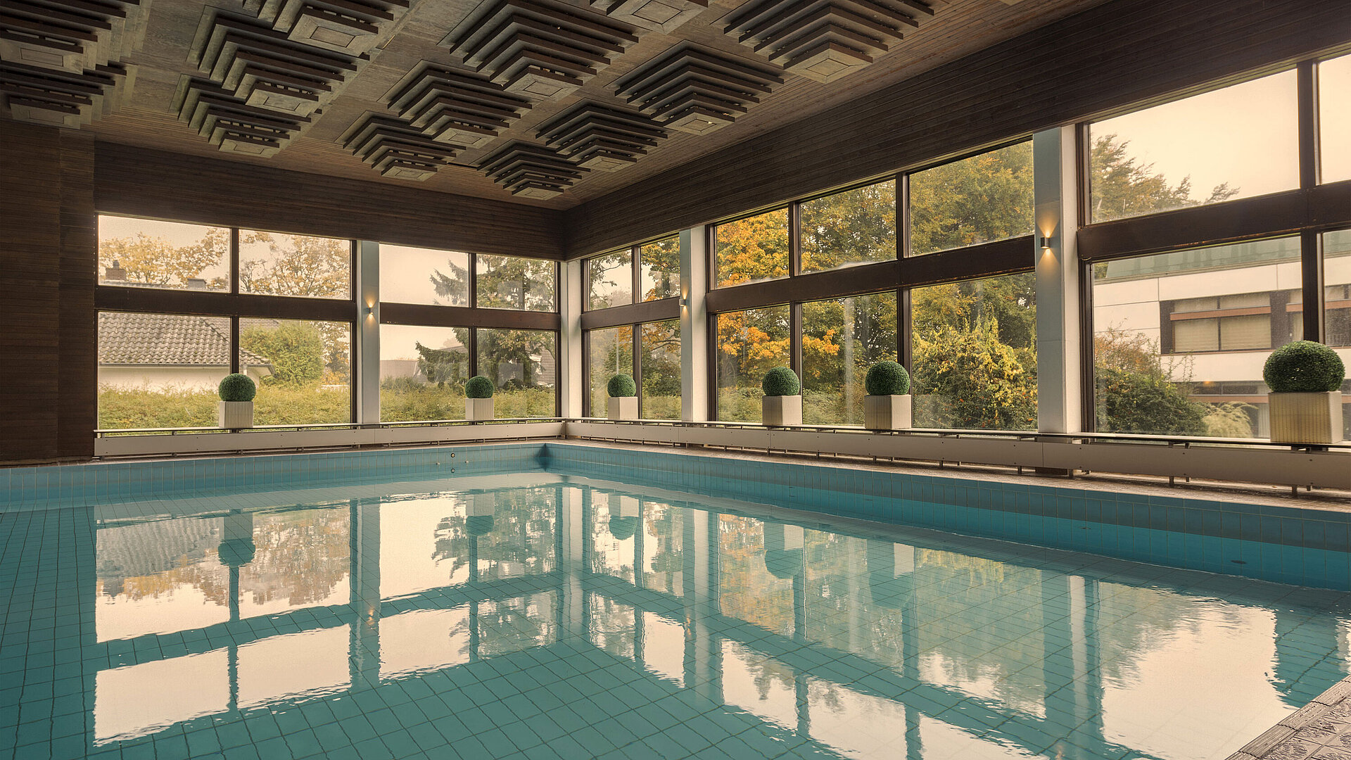 Schwimmbad Innenpool im Maritim Hotel Kiel, umgeben von großen Fenstern, die einen Blick ins Grüne ermöglichen.
