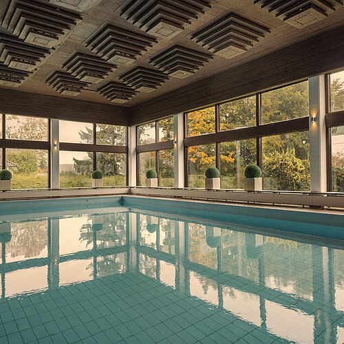 Innenpool im Maritim Hotel Kiel, umgeben von großen Fenstern, die einen Blick ins Grüne ermöglichen.