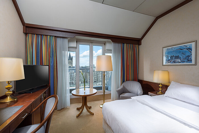 Classic Zimmer im Maritim Hotel Köln mit Doppelbett, Schreibtisch und Blick auf den Rhein sowie das historische Stadtzentrum.