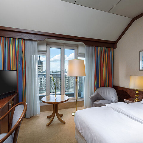 Classic Zimmer im Maritim Hotel Köln mit Doppelbett, Schreibtisch und Blick auf den Rhein sowie das historische Stadtzentrum.