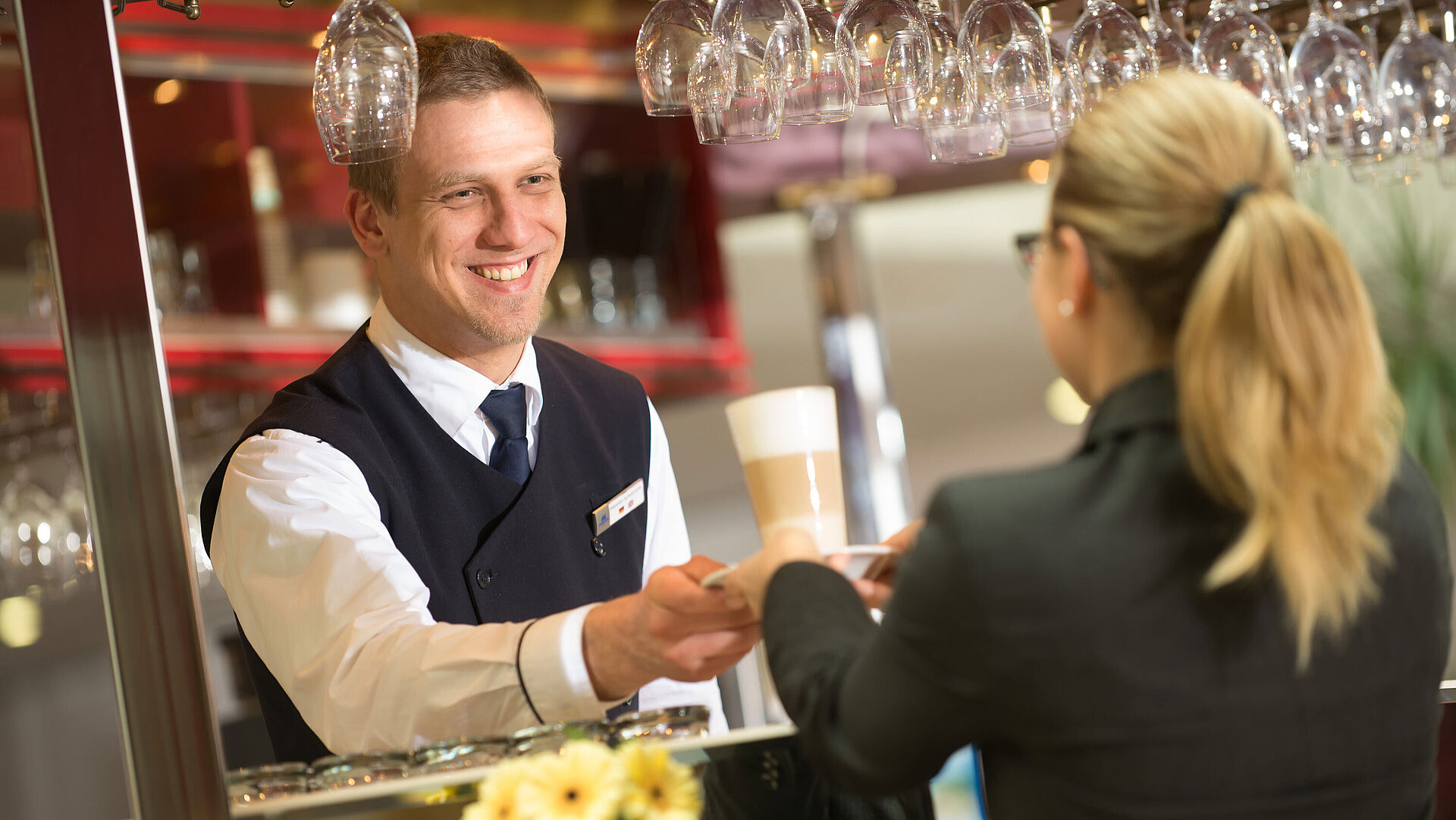 Ein Barkeeper reicht einem Gast ein Getränk an der Bar im Maritim Hotel mit lächelndem Service.
