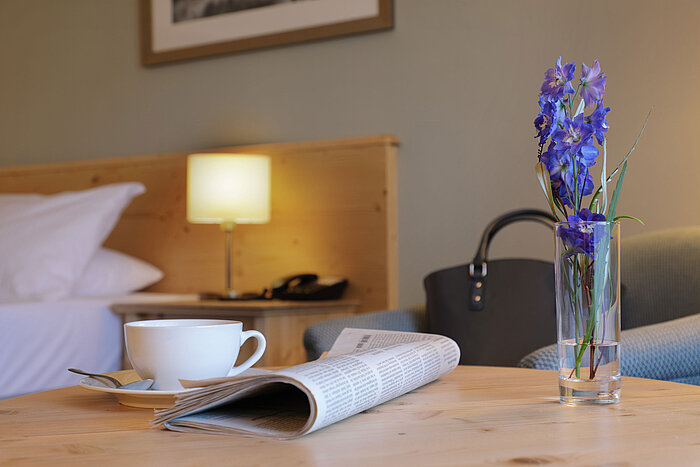 Tasse Kaffee, Zeitung und Blume auf Tisch im Zimmer des Maritim Hotel Titisee