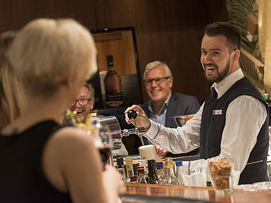 Freundlicher Barkeeper serviert ein Getränk an der Bar des Maritim Hotel Bad Salzuflen mit lächelnden Gästen