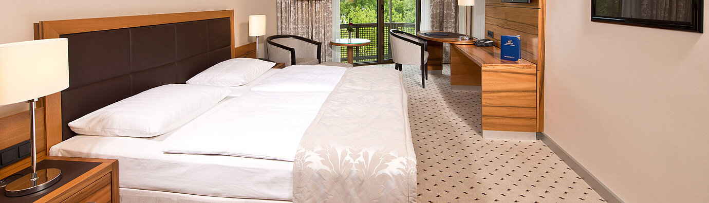 Helles Zimmer im Maritim Hotel Bad Homburg mit gemütlichem Bett, Schreibtisch und Balkon mit grünem Ausblick.
