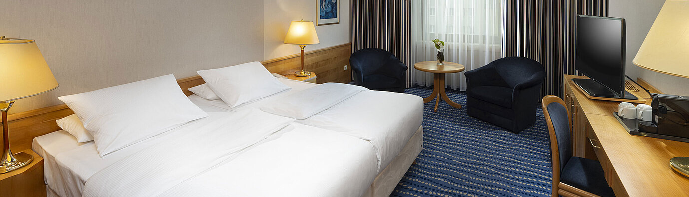 Superior Zimmer Großes Bett mit Nachttischen und Lampen, daneben Sitzbereich und Schreibtisch.