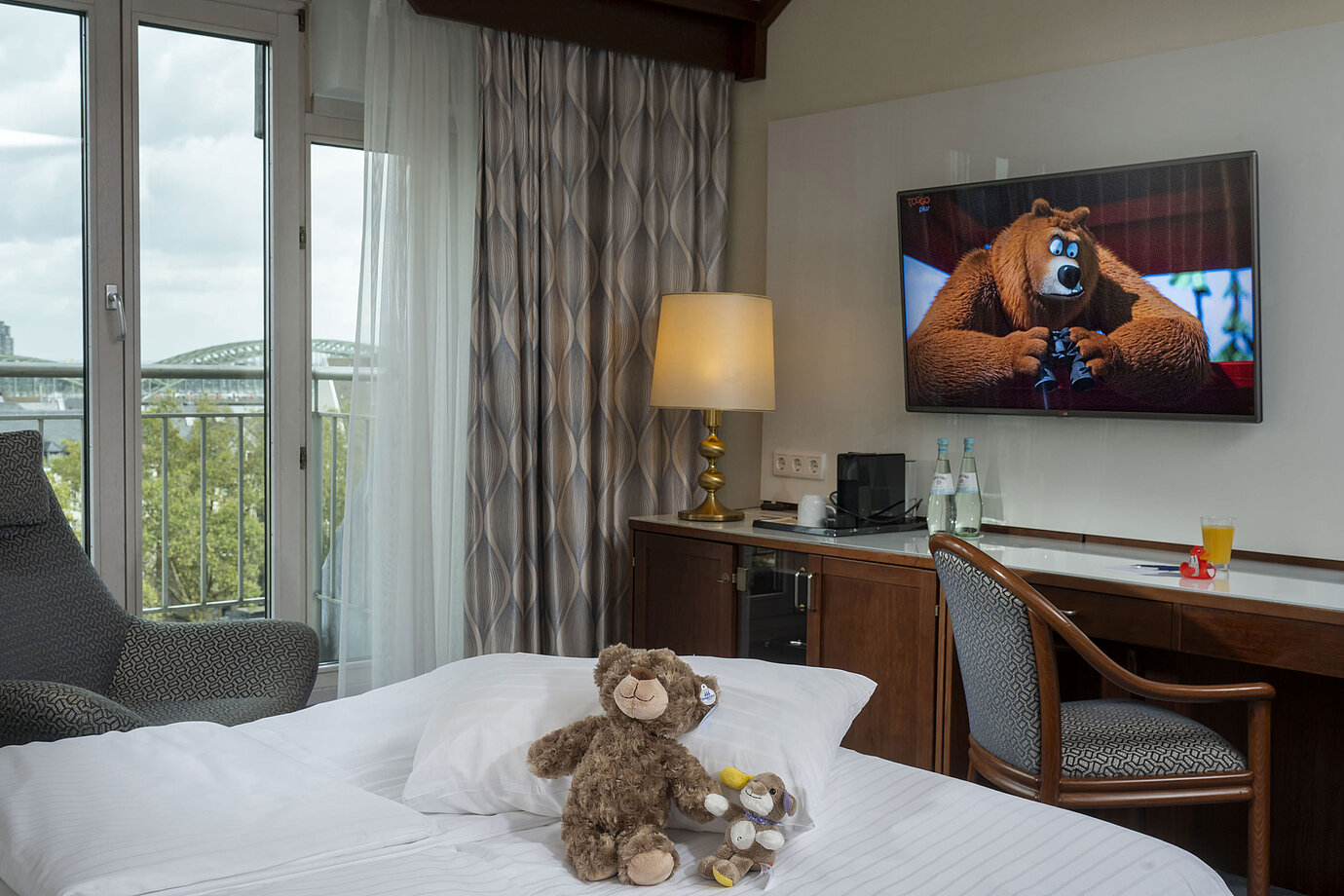 Familienzimmer im Maritim Hotel Köln mit TV, gemütlichen Kuscheltieren auf dem Bett und Blick auf den Rhein.