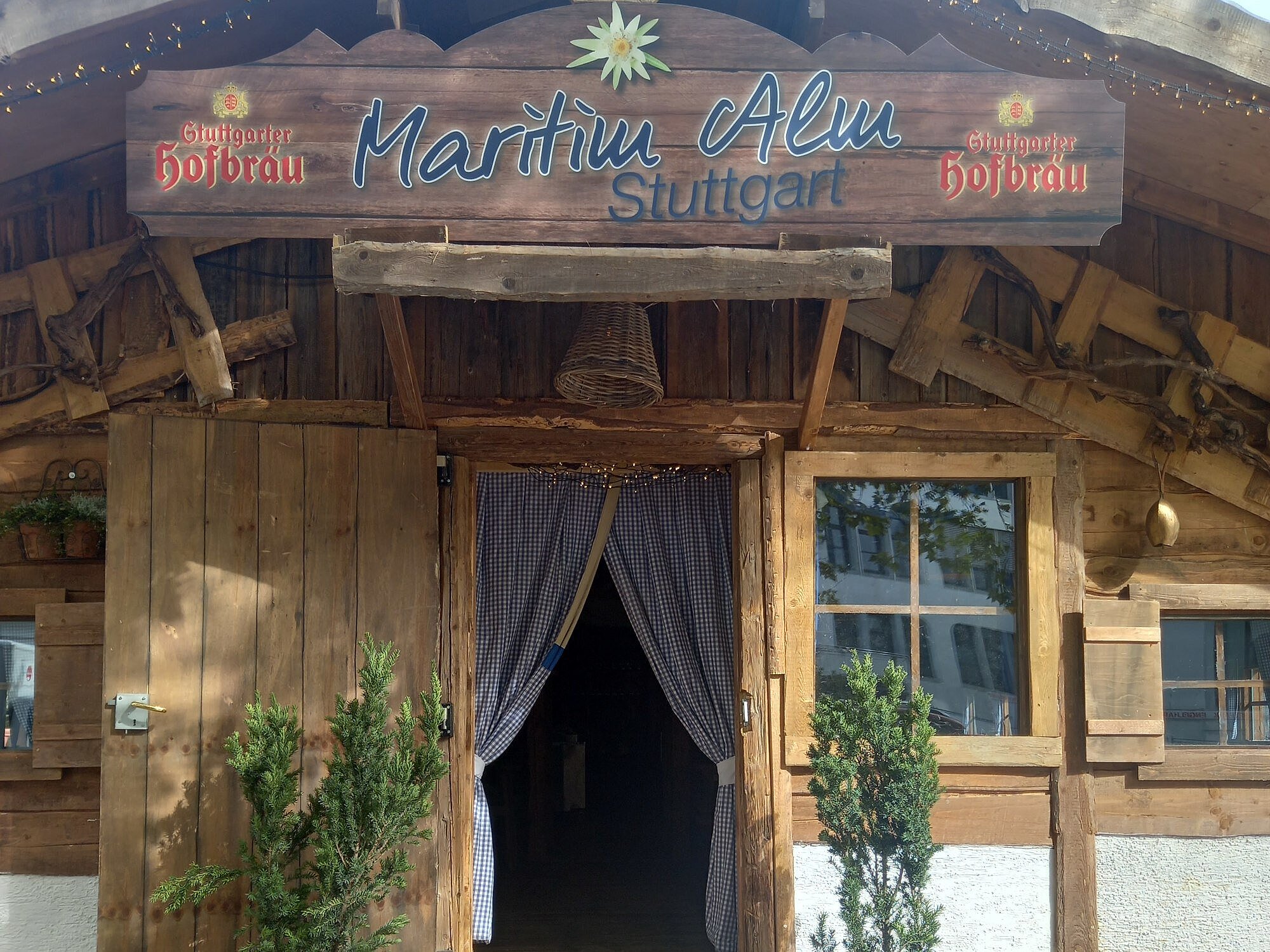 Eingang mit Holzfassade und Vorhängen zur Maritim Alm neben dem Maritim Hotel Stuttgart