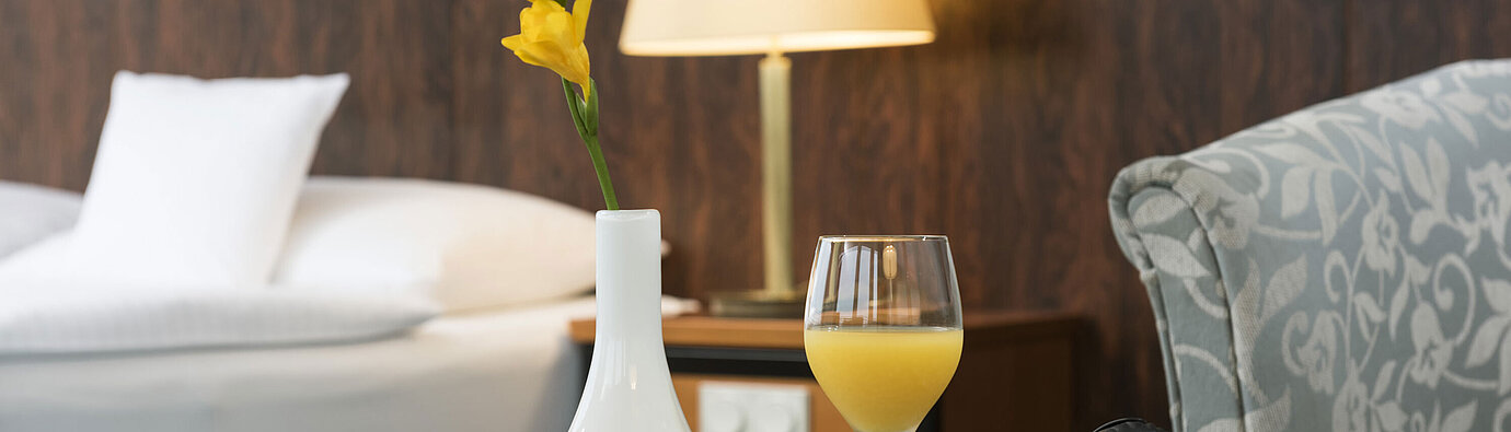 Zimmerdetail Details eines Zimmers im Maritim Hotel Kiel: Glas Orangensaft, Kopfhörer und Vase auf dem Tisch, im Hintergrund ein Bett.