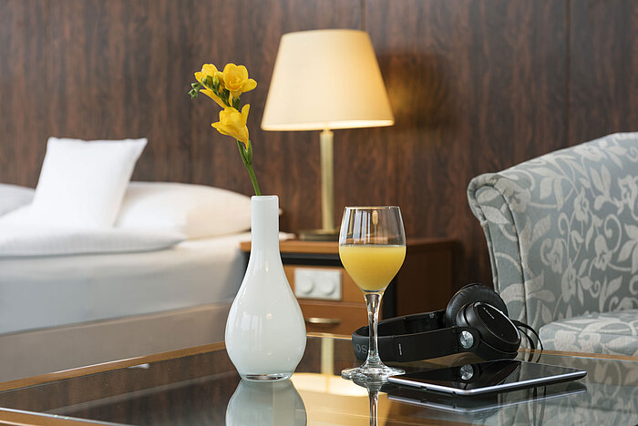Zimmerdetail Details eines Zimmers im Maritim Hotel Kiel: Glas Orangensaft, Kopfhörer und Vase auf dem Tisch, im Hintergrund ein Bett.