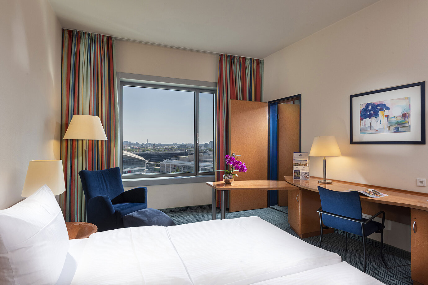 Comfort Familienzimmer im Maritim Hotel Frankfurt mit Doppelbett, Schreibtisch, bunten Vorhängen und Blick auf die Stadt.