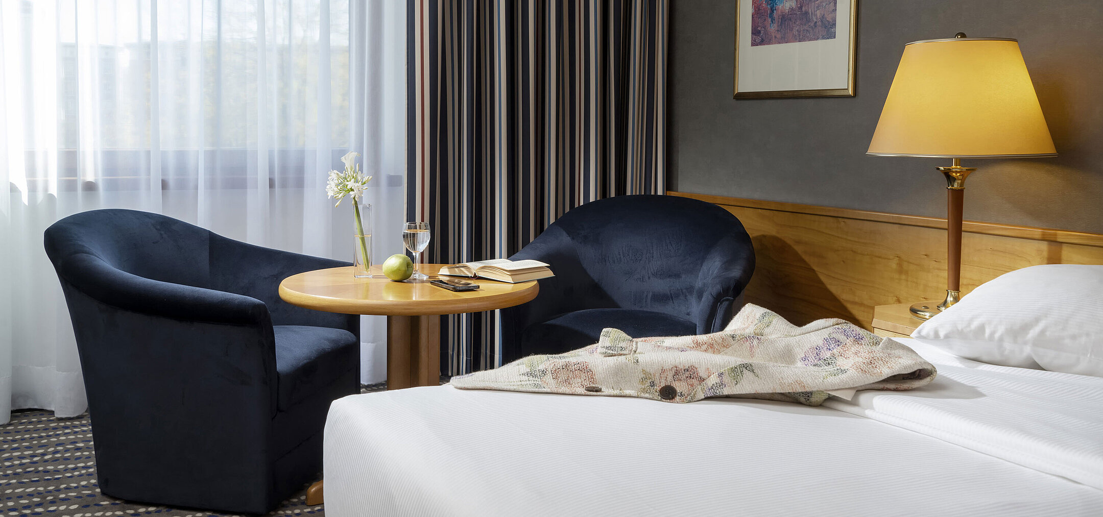 Sitzecke im Hotelzimmer mit Tisch, Buch, Glas Wasser und Apfel, perfekt zum Entspannen