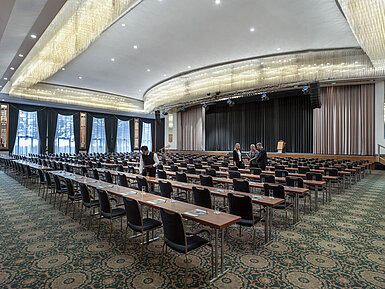 Prächtiger Saal im Maritim Hotel Magdeburg mit Bühne, Reihenbestuhlung und luxuriösem Kronleuchter.