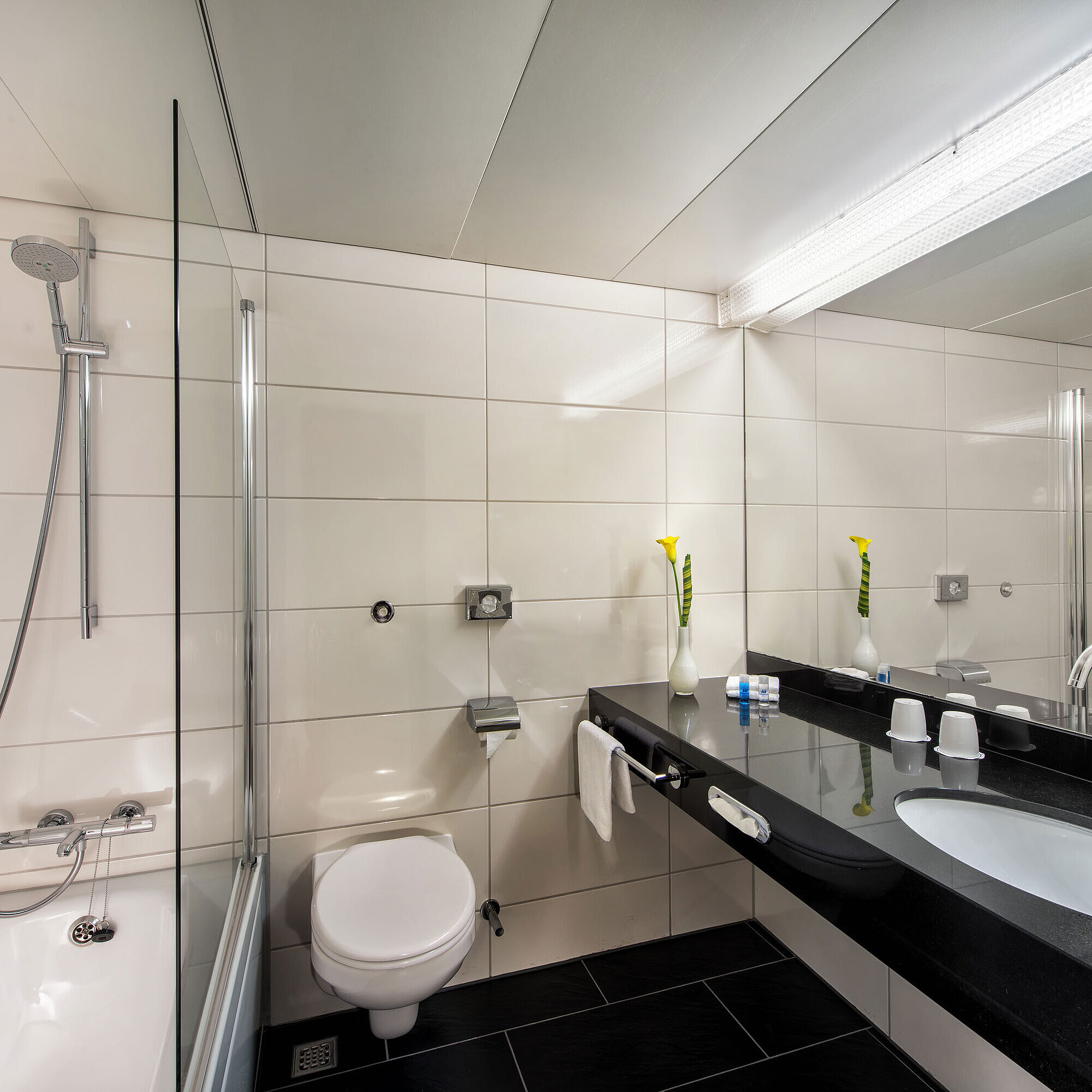 Badezimmer Badezimmer im Maritim Hotel Kiel mit Badewanne, Glasduschwand, Waschbecken und großem Spiegel auf schwarzer Ablage.