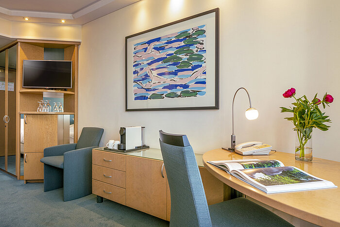 Modern eingerichtetes Superior-Zimmer im Maritim proArte Hotel Berlin mit Schreibtisch, Kunstwerk, Sessel und Kaffeemaschine.