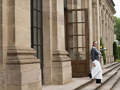 Maritim Service Freundliche Servicekraft serviert Frühstück mit frisch gepresstem Orangensaft auf der Terrasse des Maritim Hotel Fulda.