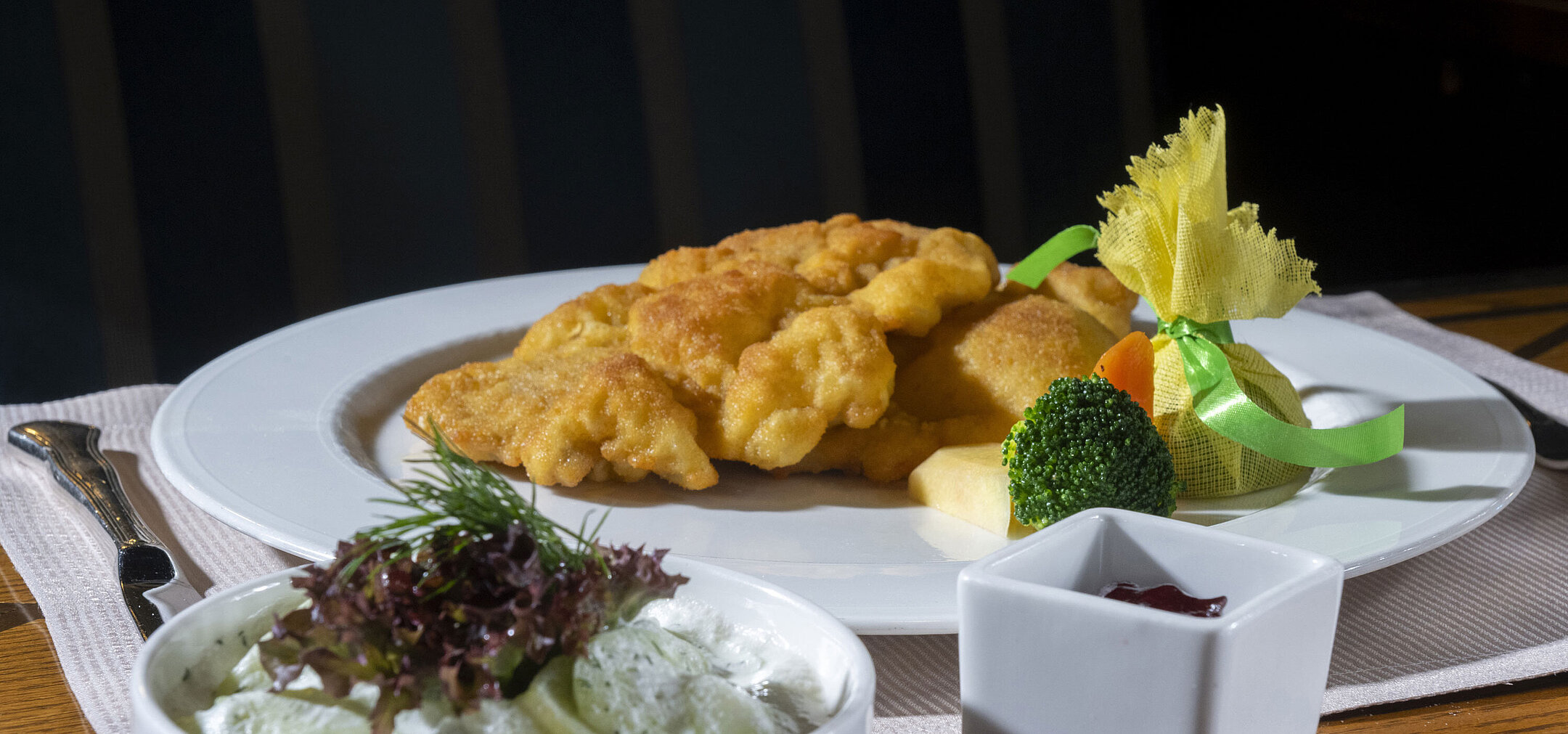 Wiener Schnitzel mit klassischen Beilagen Knuspriges Wiener Schnitzel mit Gurkensalat, Preiselbeeren und Gemüse auf elegant angerichtetem Teller