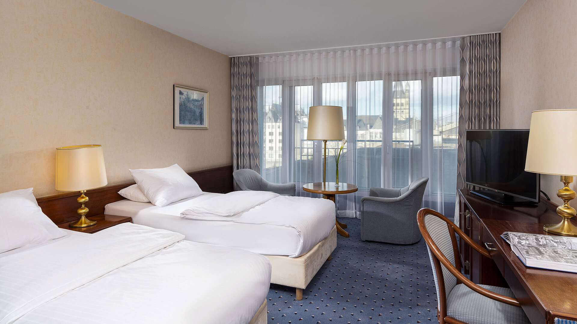 Standard-Twin Zimmer im Maritim Hotel Köln mit zwei Betten, Sitzbereich, Schreibtisch, Flachbildfernseher und großen Fenstern