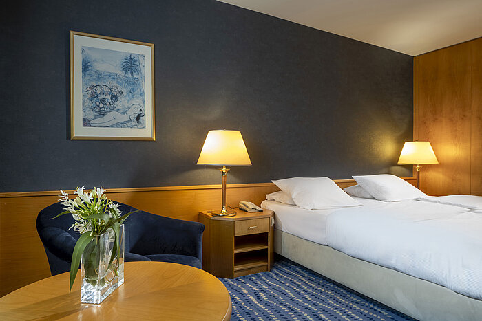 Hotelzimmer mit Doppelbett, gemütlicher Sitzecke und Blumen auf dem Tisch, ideale Atmosphäre zum Entspannen