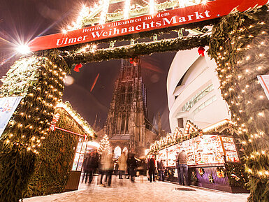 Eingang Ulmer Weihnachtsmarkt mit beleuchteten Ständen und Münster im Hintergrund