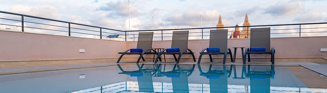 Rooftop-Pool mit Sonnenliegen und Blick über die Stadt bei blauem Himmel