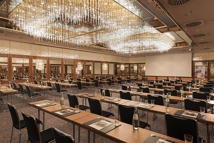 Großzügiger Konferenzsaal mit Kristallleuchtern und gespannter Atmosphäre im Maritim Hotel München