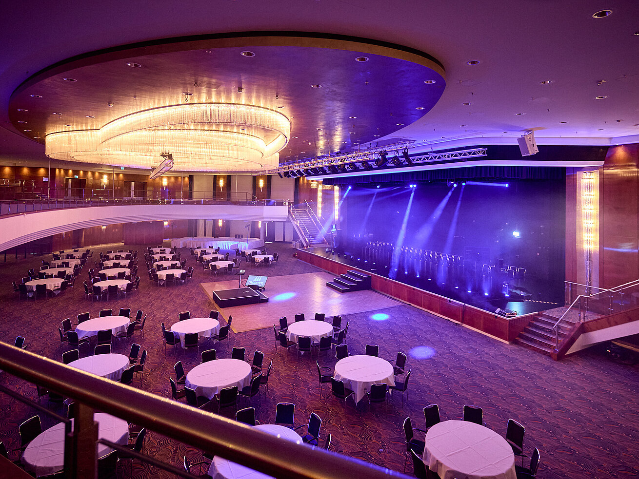Festlich beleuchteter Ballsaal für Events Großer Ballsaal mit Bühne, runden Tischen und moderner Lichttechnik für Gala oder Tagung.