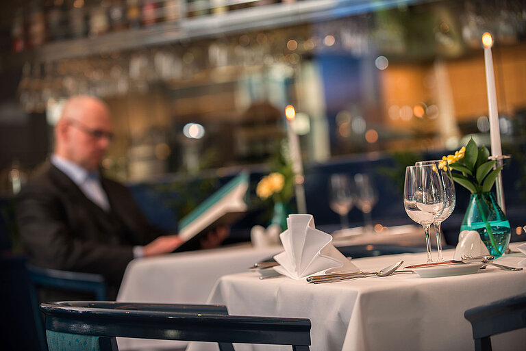 Eleganter gedeckter Tisch im Restaurant des Maritim Hotel Magdeburg mit einem Gast beim Studieren der Speisekarte.