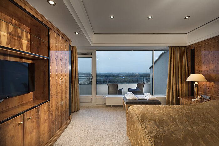 Penthouse-Schlafzimmer mit Holzmöbeln, großer Fensterfront und Balkonblick im Maritim Seehotel Timmendorfer Strand.