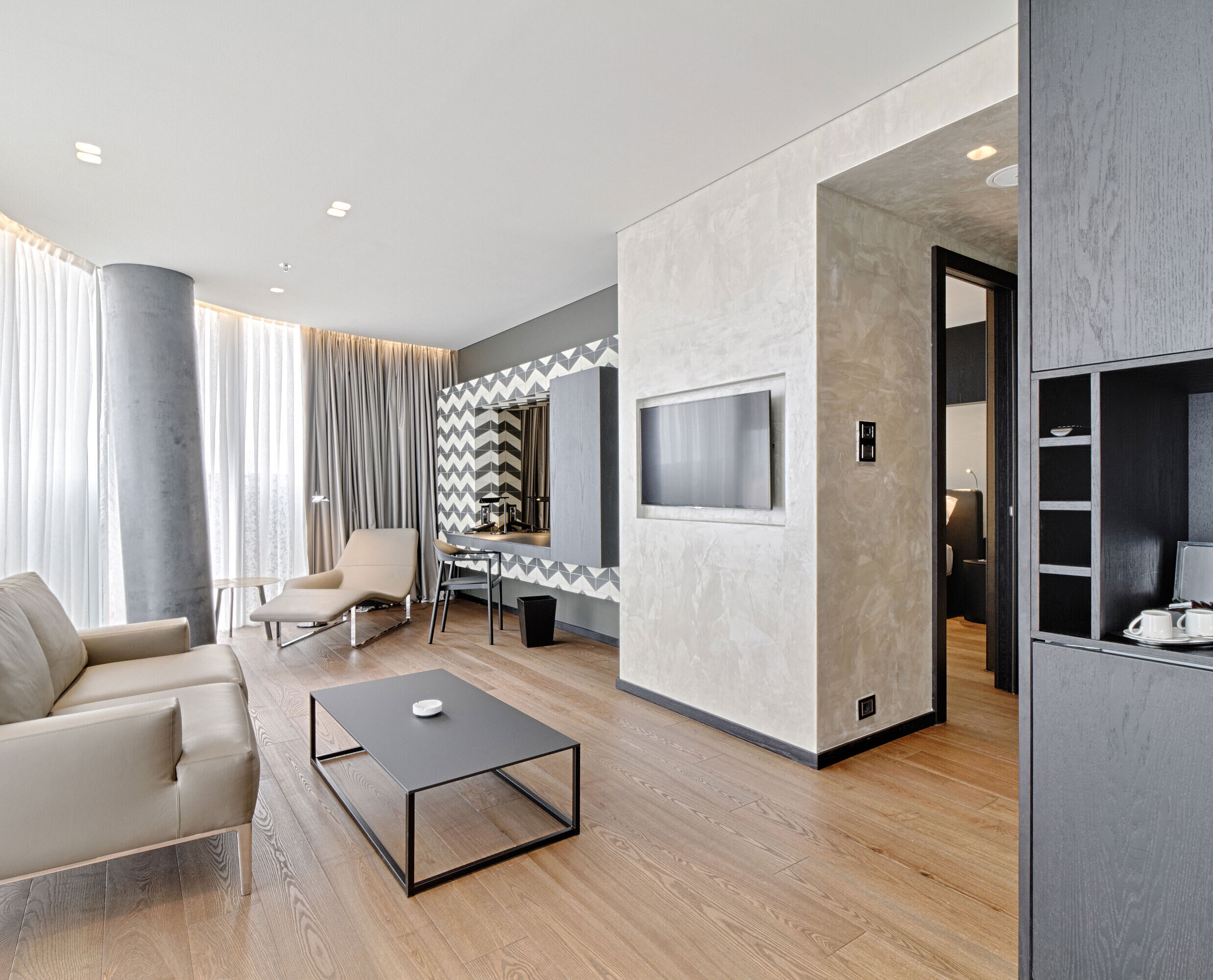 Suite Lounge mit Sofa, TV, Designspiegel und Relaxliege im Maritim Hotel Plaza Tirana mit Tageslicht