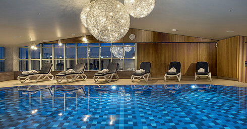 Schwimmbad mit blauen Fliesen und Liegen im Maritim Hotel München