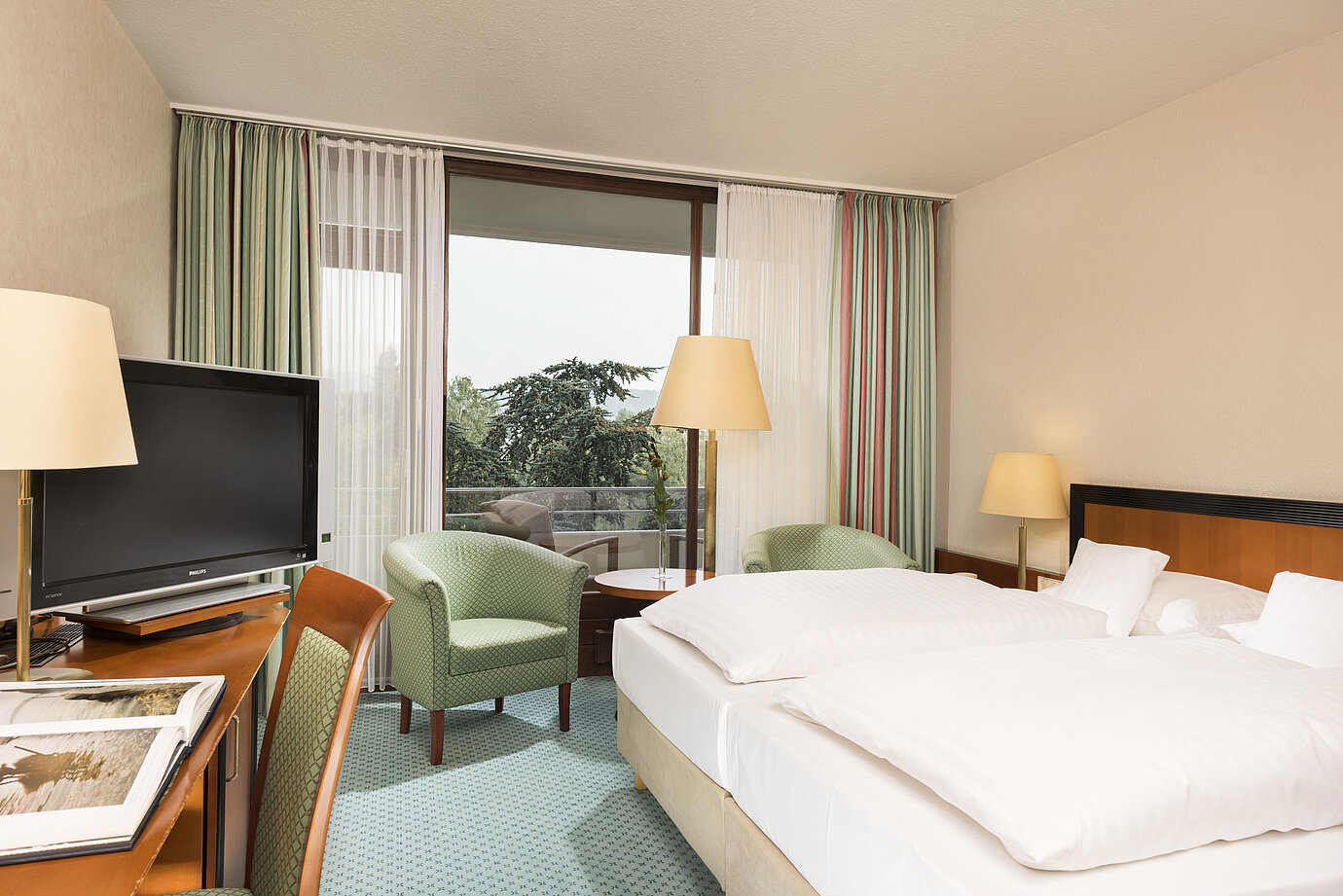 Helles Hotelzimmer im Maritim Hotel Bad Salzuflen mit Doppelbett, Sitzbereich und Zugang zum Balkon mit Ausblick