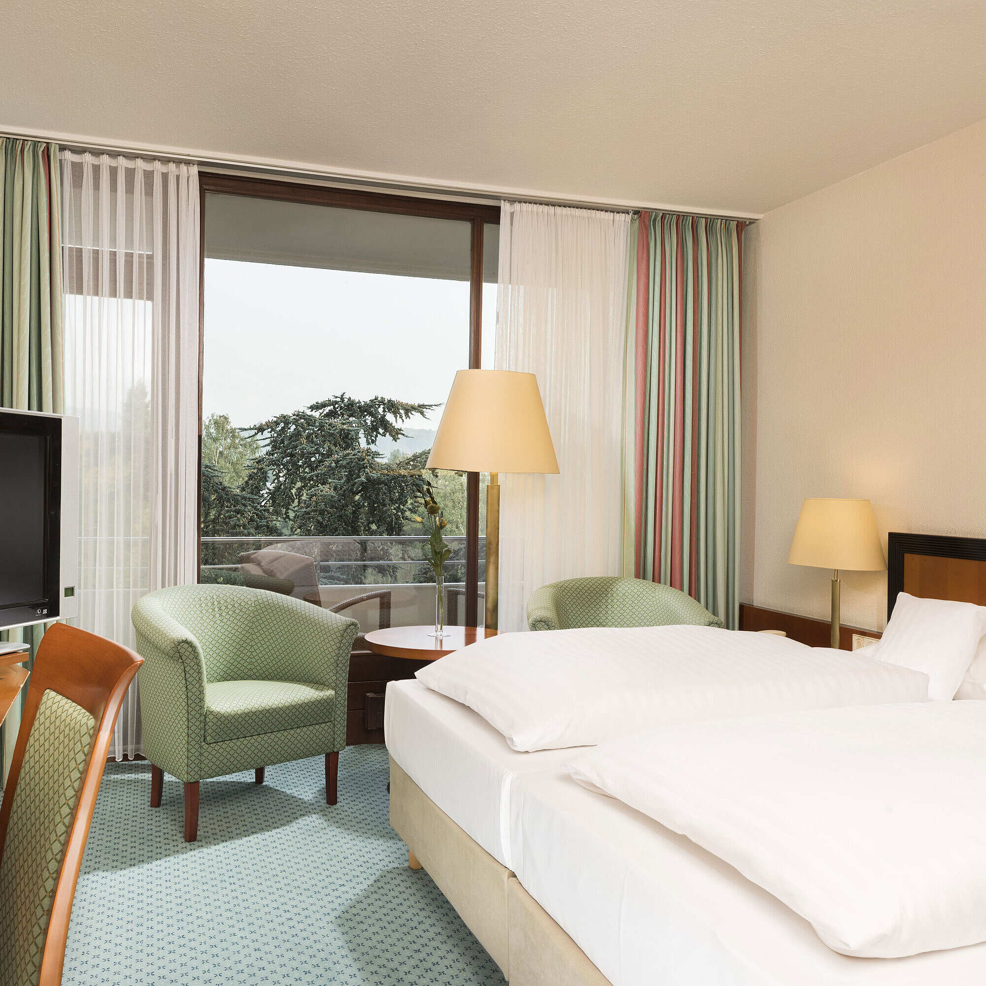 Helles Hotelzimmer im Maritim Hotel Bad Salzuflen mit Doppelbett, Sitzbereich und Zugang zum Balkon mit Ausblick