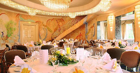 Eleganter Bankettsaal mit Wandmalerei, Kronleuchtern und festlich gedeckten Tischen