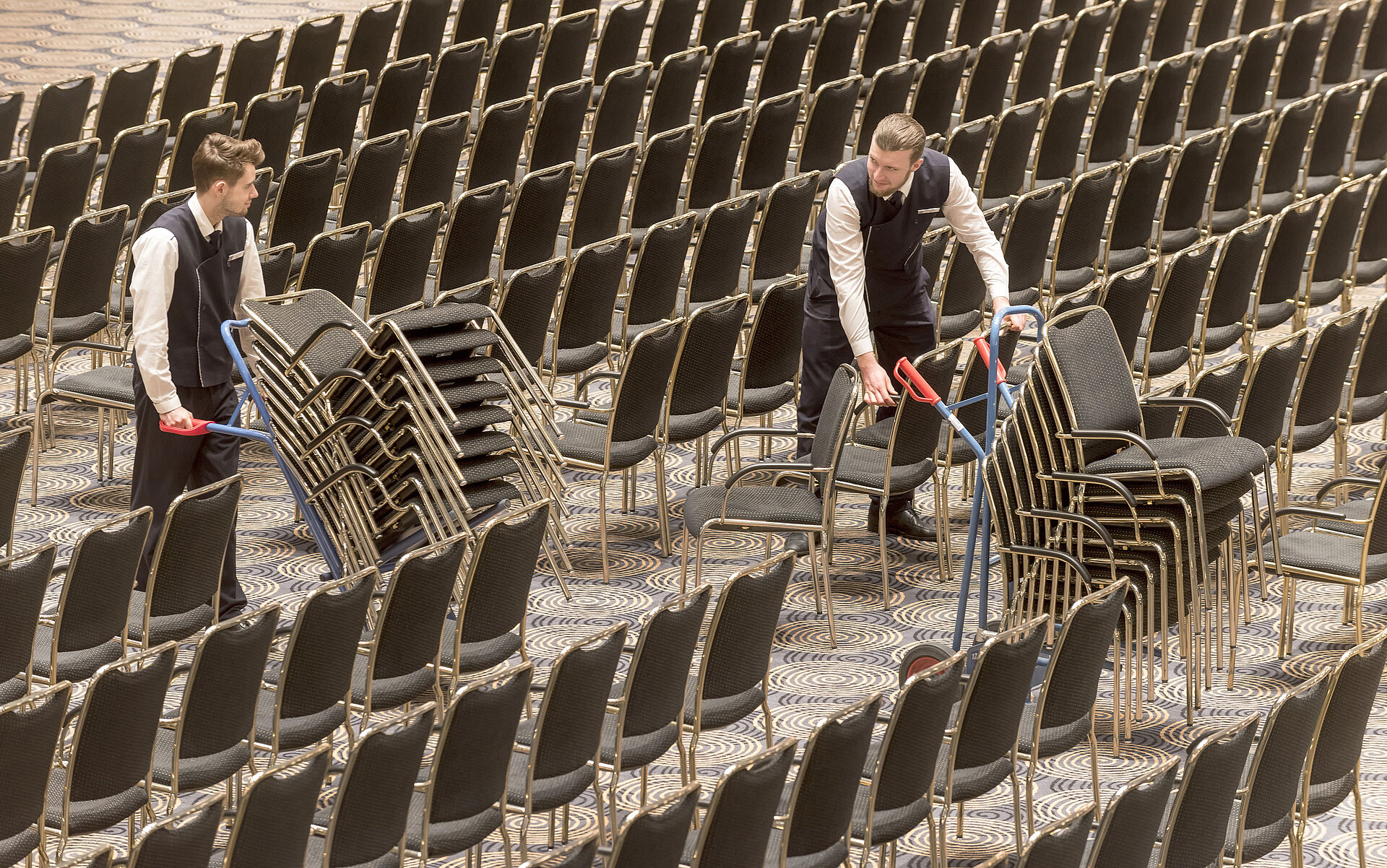 Mitarbeiter richten den Saal Maritim im Maritim Hotel Bonn ein und stapeln Stühle für eine Veranstaltung.