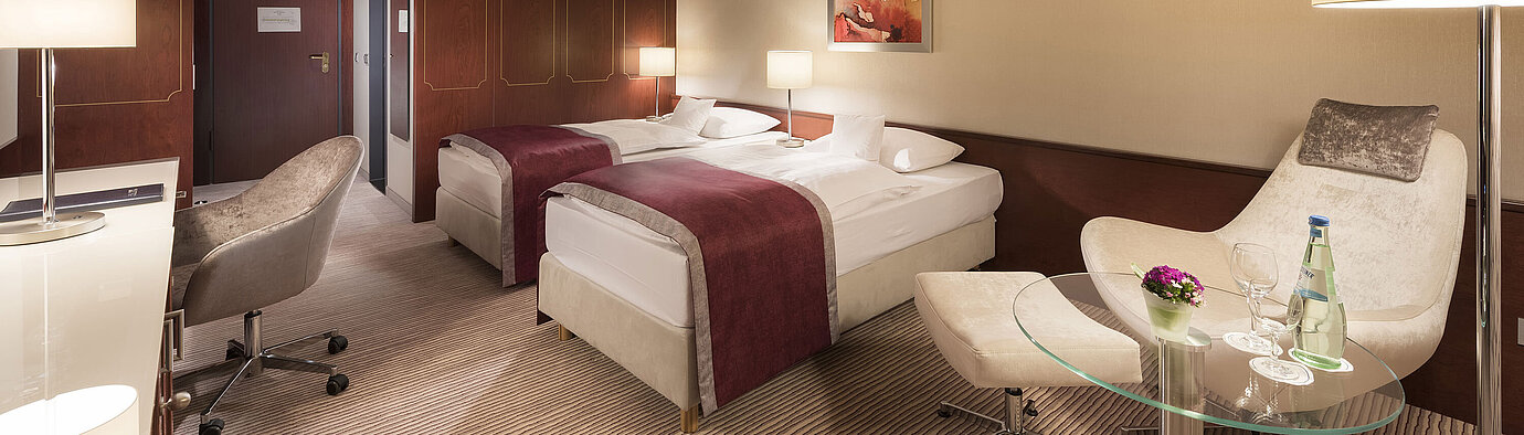 Comfort Zimmer im Maritim Hotel Bonn, ausgestattet mit zwei Einzelbetten, Sessel, Schreibtisch und moderner Beleuchtung.