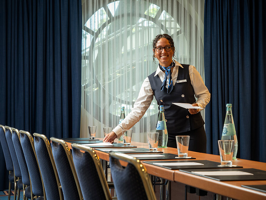 Mitarbeiterin im Maritim Hotel Köln bereitet Konferenzraum mit Getränken und Unterlagen vor