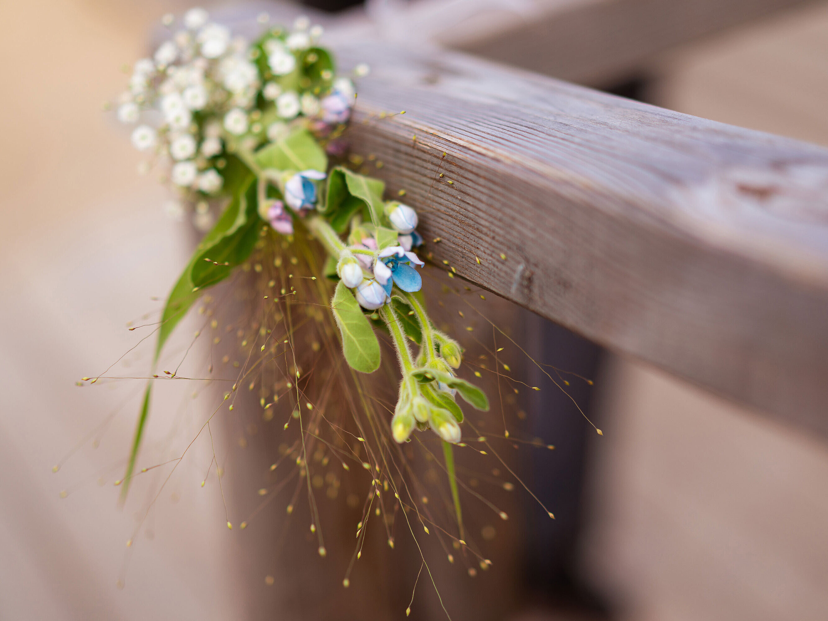 Zartes Blumenarrangement mit kleinen weißen Blüten und grünen Blättern, dekorativ an einem Holzgeländer befestigt.