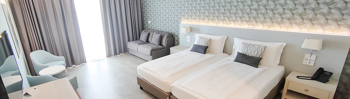Großzügiges Zimmer im Maritim Resort Calabria mit Twin-Bett, Sofa, Schreibtisch und hellen Farben
