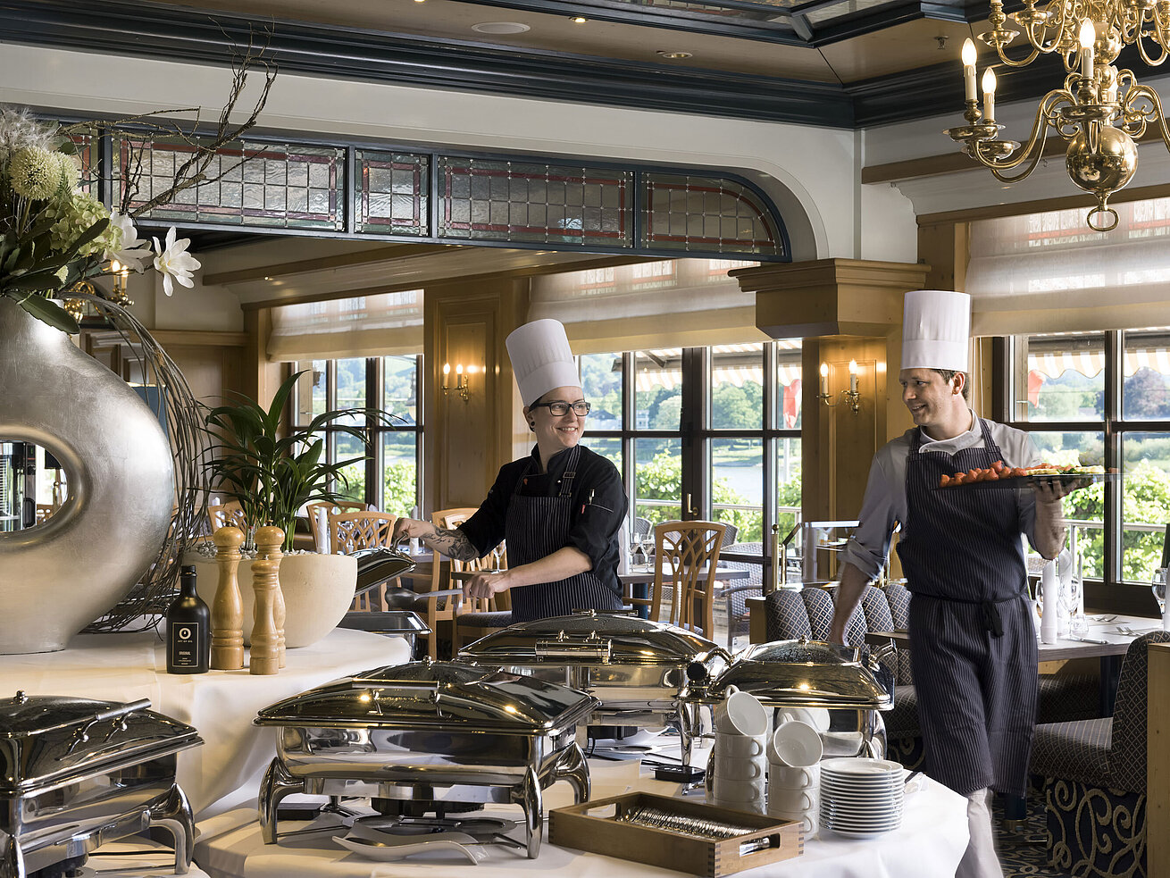 Zwei Köche am Buffet des Maritim Hotel Königswinter bereiten frisch angerichtete Speisen mit Blick auf den Rhein zu.