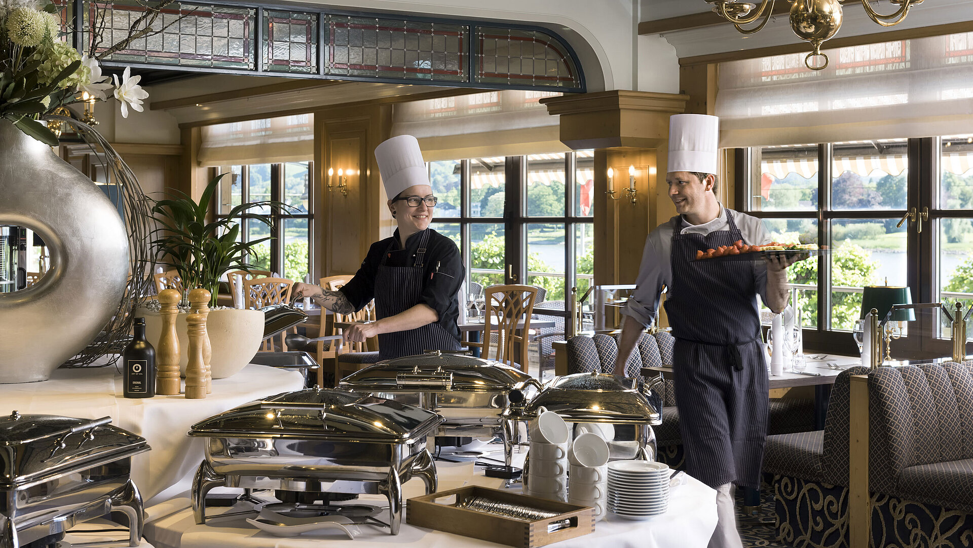 Zwei Köche am Buffet des Maritim Hotel Königswinter bereiten frisch angerichtete Speisen mit Blick auf den Rhein zu.