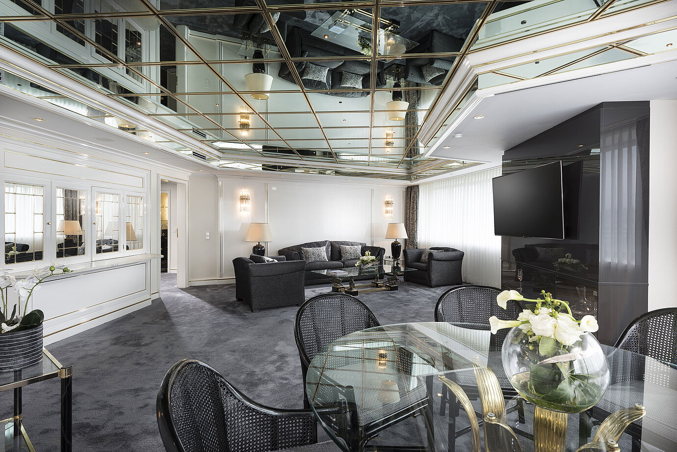 Stilvolles Wohnzimmer der Luxus-Suite im Maritim Hotel Bonn mit Spiegeldecke, modernen Möbeln und einem großen Esstisch.